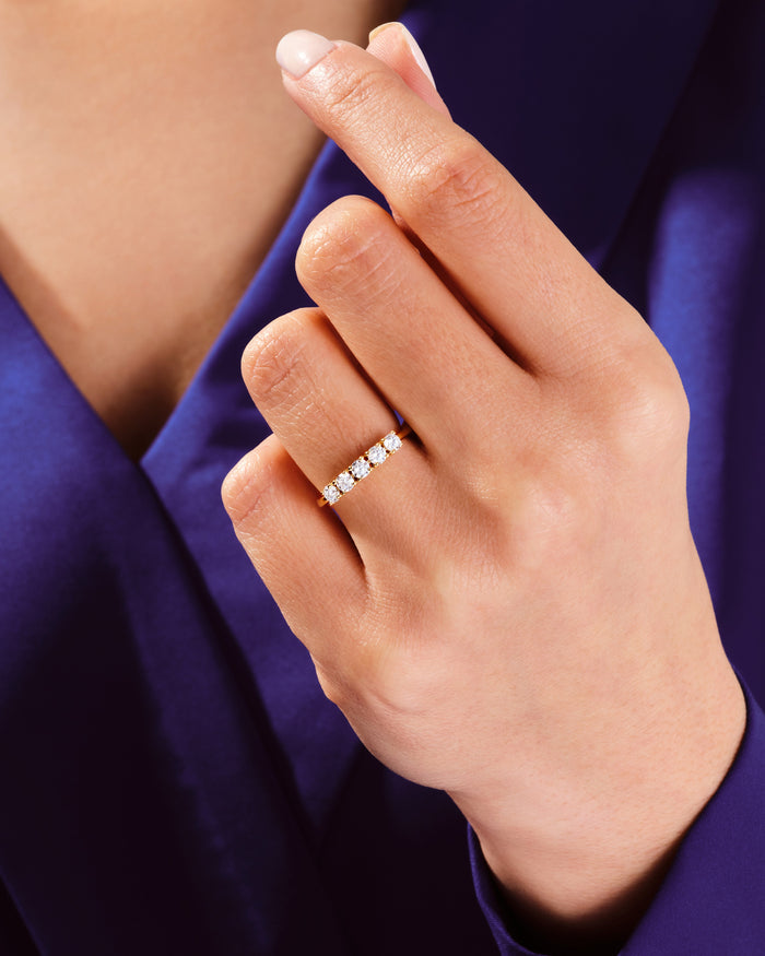 Five stone moissanite basket band in yellow gold worn on a hand