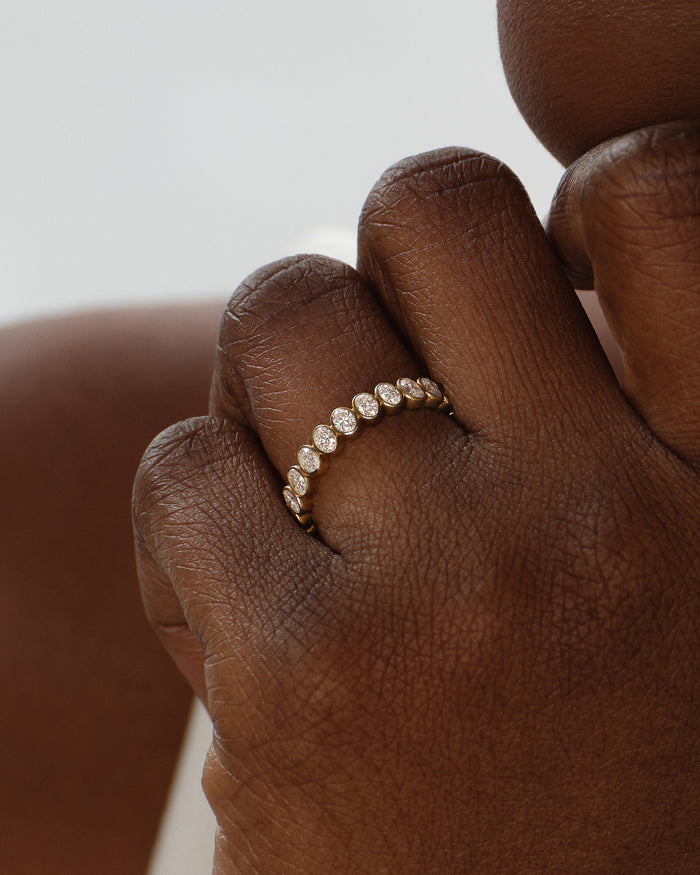 Oval bezel eternity band in yellow gold worn on the finger, close view