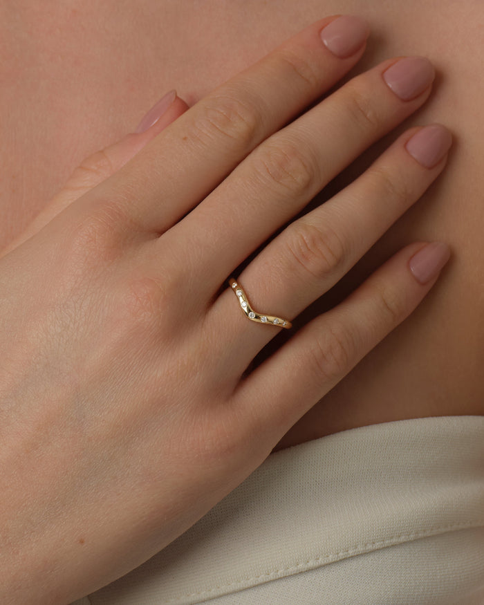 Flush set curved moissanite wedding band worn on a hand in yellow gold