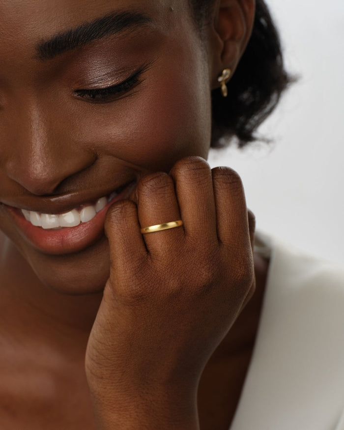 3mm matte brushed dome gold wedding band worn on a hand near the face