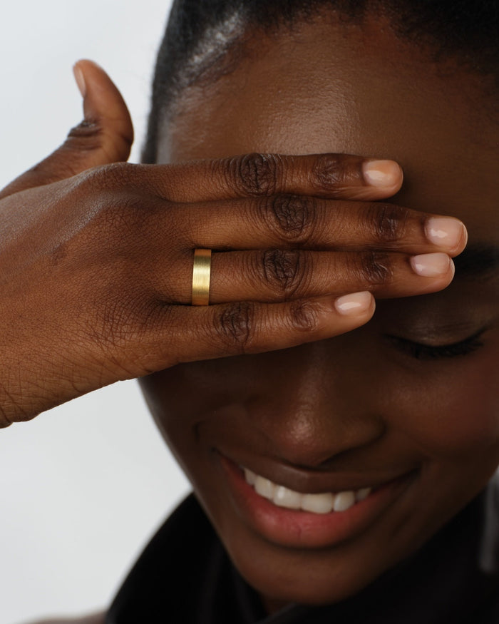 6mm flat matte brushed gold wedding band worn on a hand covering the eye