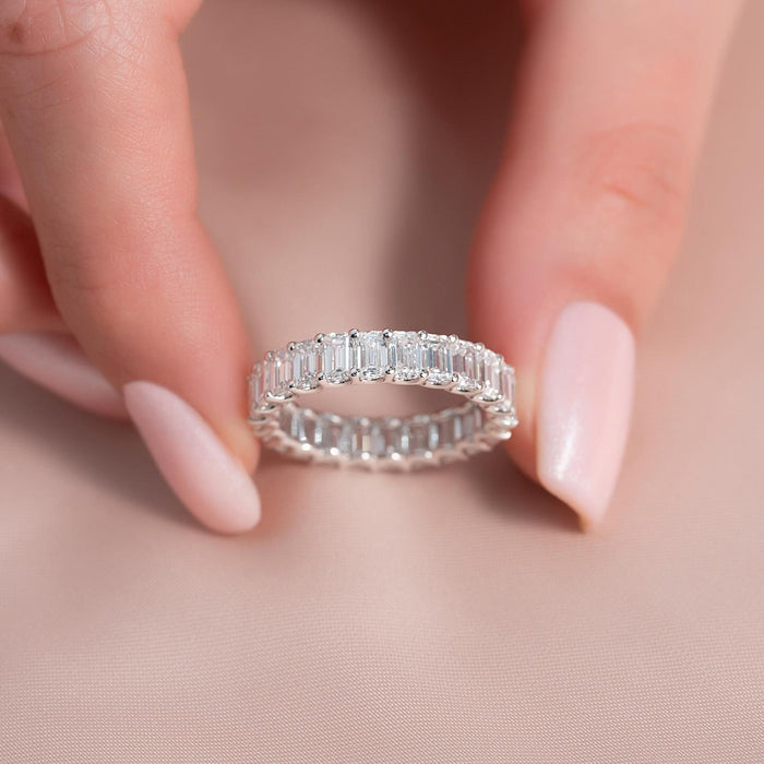 Emerald cut moissanite eternity band held in fingers