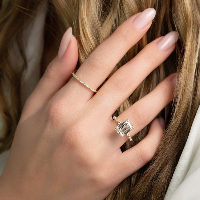 Emerald cut lab grown diamond ring with hidden halo and graduated round band in yellow gold worn on the hand