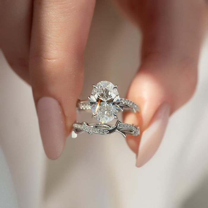 Oval moissanite hidden halo vine bridal set in white gold held in fingers