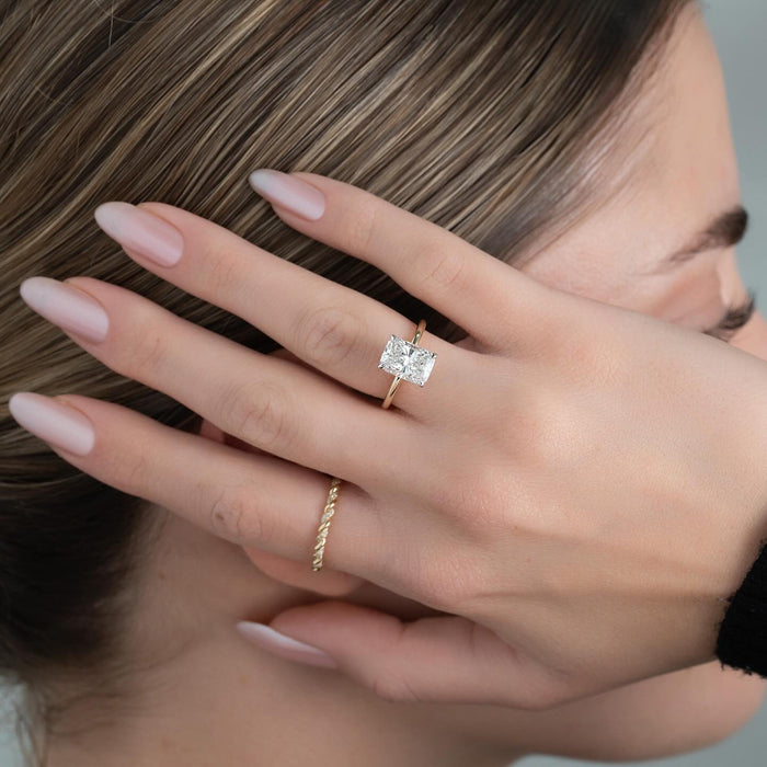 Elongated radiant cut lab grown diamond solitaire ring on a plain yellow gold band worn on the hand