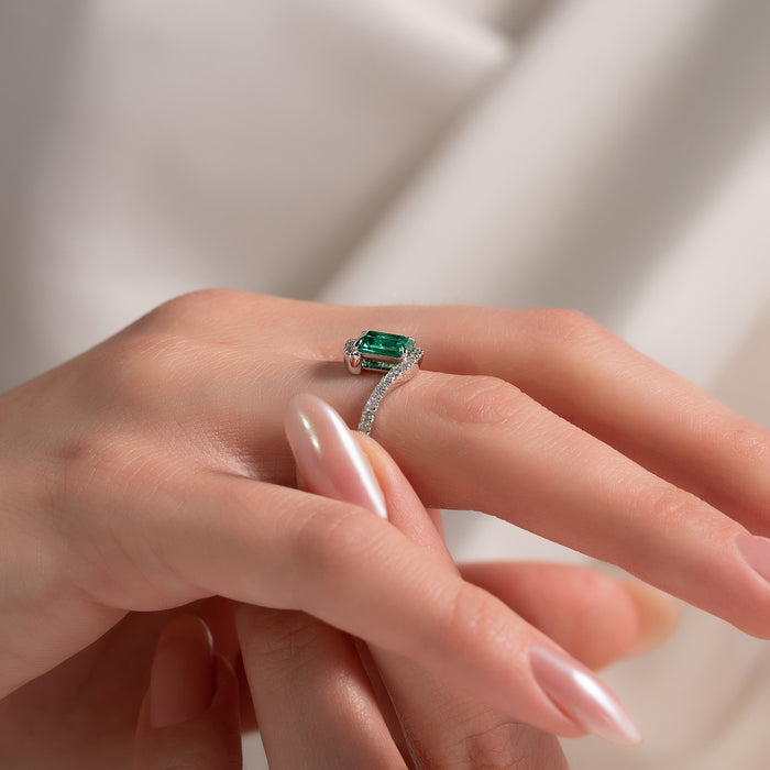 Pave band sweeping diagonally past the green emerald centre stone