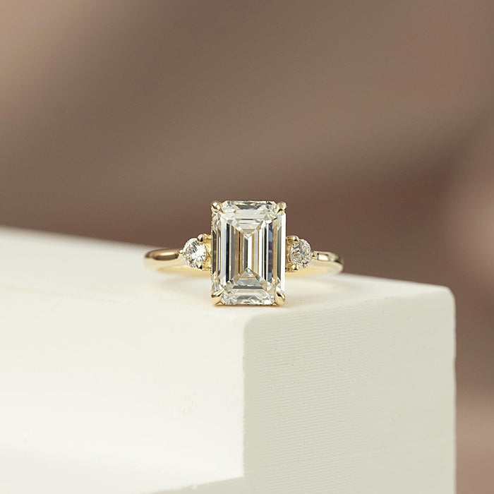 Emerald cut lab grown diamond three stone ring in yellow gold with round brilliant side stones