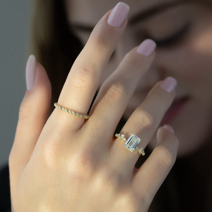 Scattered accent clusters along the shoulder of the emerald cut ring