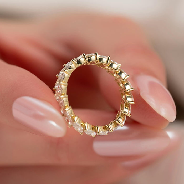 Marquise moissanite slanted full eternity band held in fingers in yellow gold