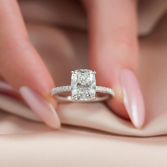 Elongated cushion moissanite ring held in fingers with pave band