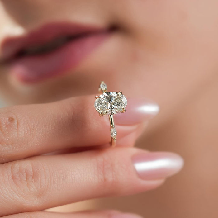 Oval moissanite hidden halo marquise side accent ring held in fingers in yellow gold