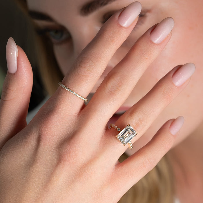 Emerald cut moissanite ring on hand showing accent band in yellow gold