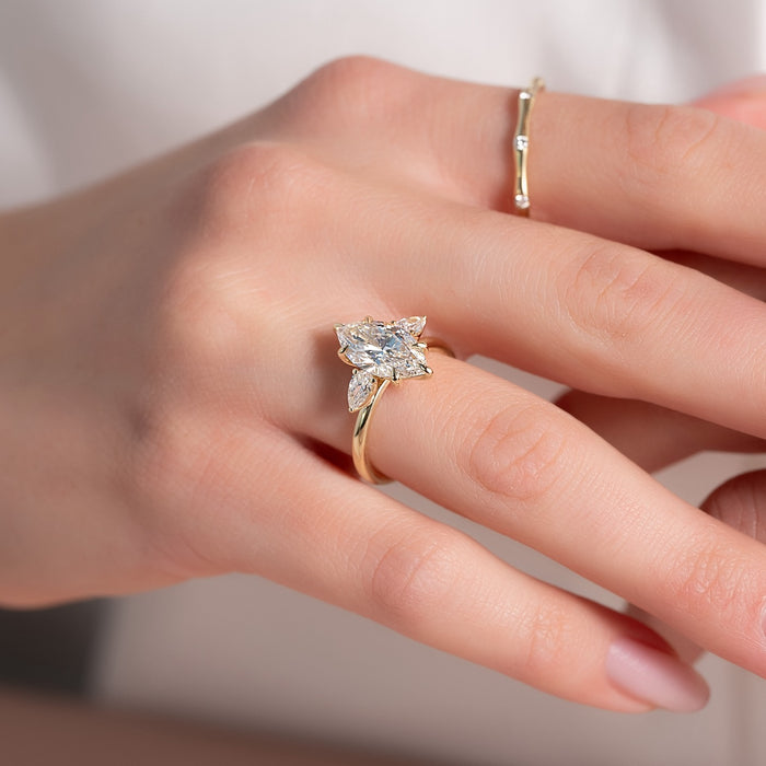 Marquise moissanite three stone ring with pear accents worn on hand in yellow gold