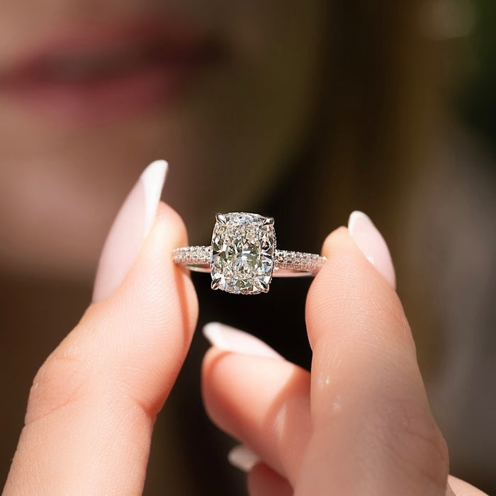 Elongated cushion moissanite hidden halo pave ring held in fingers in white gold