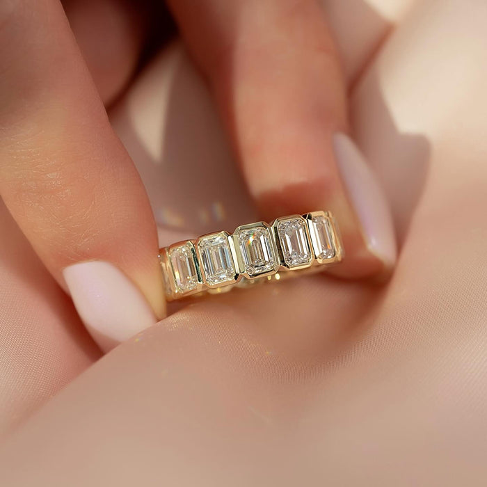 Emerald cut moissanite east west bezel eternity band front view in yellow gold