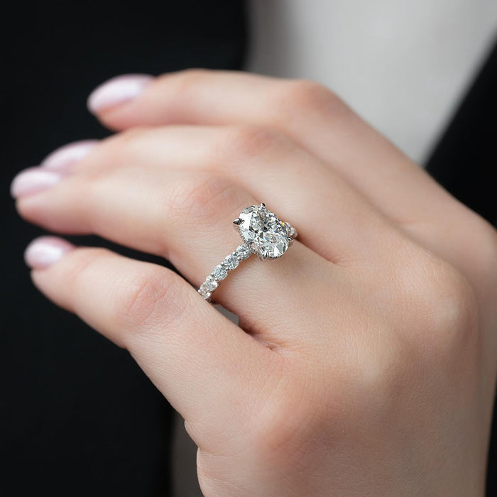 Oval moissanite ring with shared prong accent band on finger in white gold
