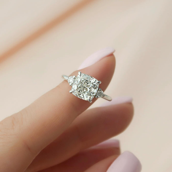 Cushion cut moissanite three stone ring with round sides held in fingers in white gold