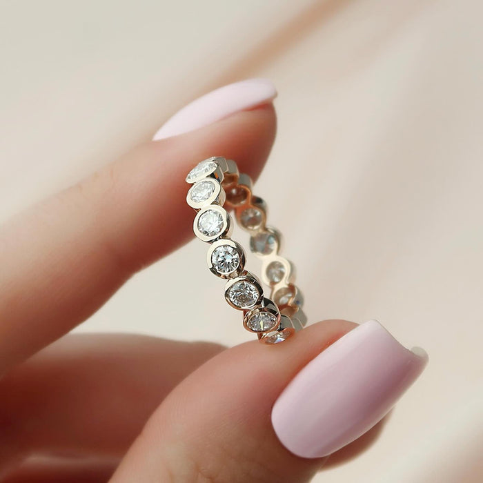Close up of round moissanite bezel eternity band held in fingers