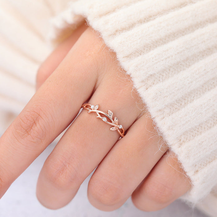 Rose gold twig and leaf moissanite wedding band worn on a finger next to a cream sweater