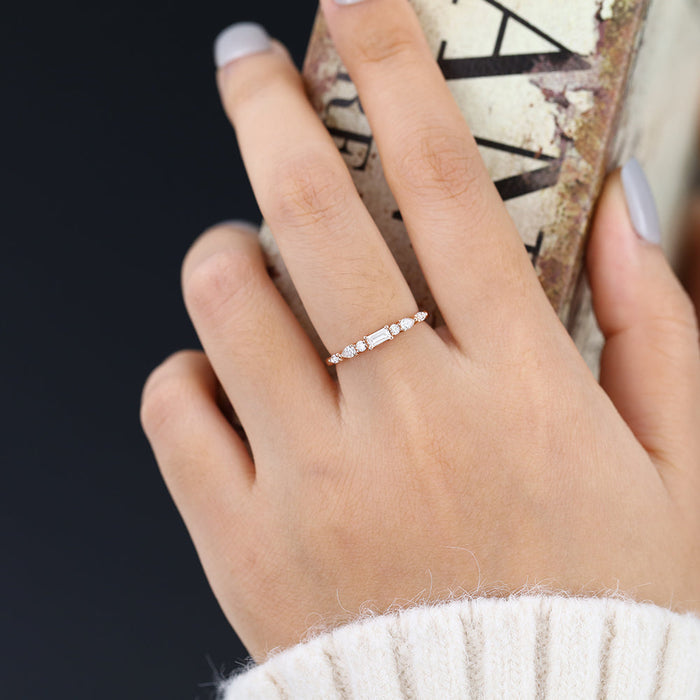 Rose gold multi stone moissanite band with a baguette center worn on a finger holding a book