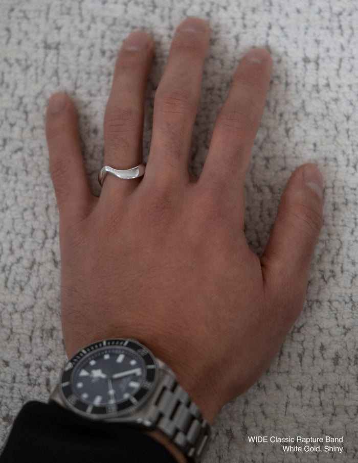 Wide plain white gold arc wedding band with a shiny finish worn on a hand
