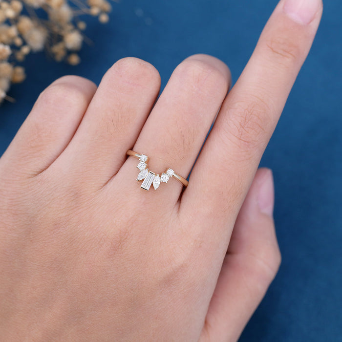 Curved cluster moissanite wedding band with round, marquise and baguette stones in yellow gold worn on a finger