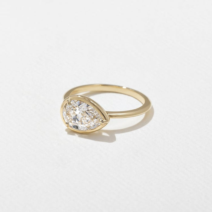 East west pear cut lab grown diamond bezel set engagement ring on a plain yellow gold band
