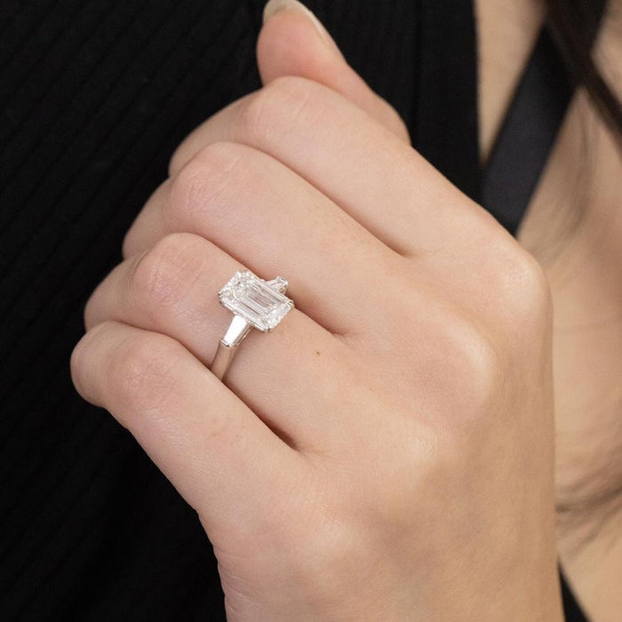 Handmade emerald cut moissanite ring with baguette side stones, angled view