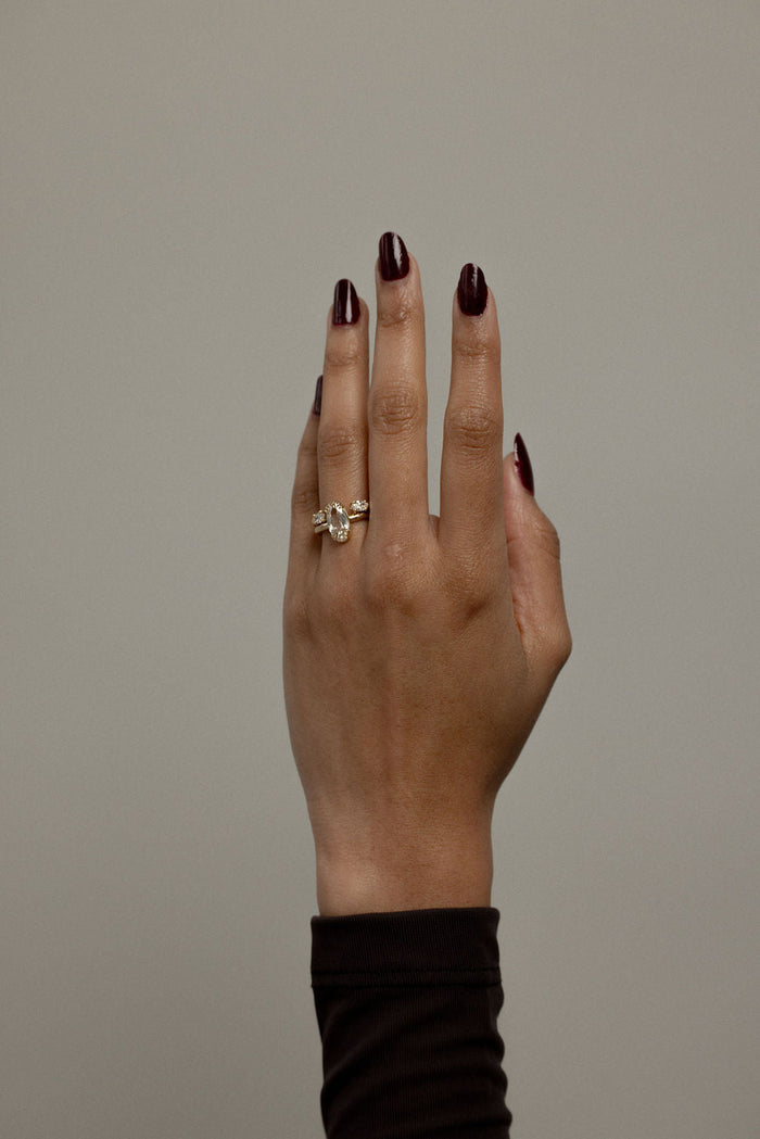 Hand raised wearing an oval moissanite open shank band stacked with a gold ring