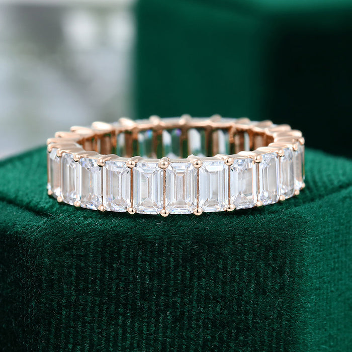Front view of a rose gold full eternity band with emerald cut moissanite stones on green velvet