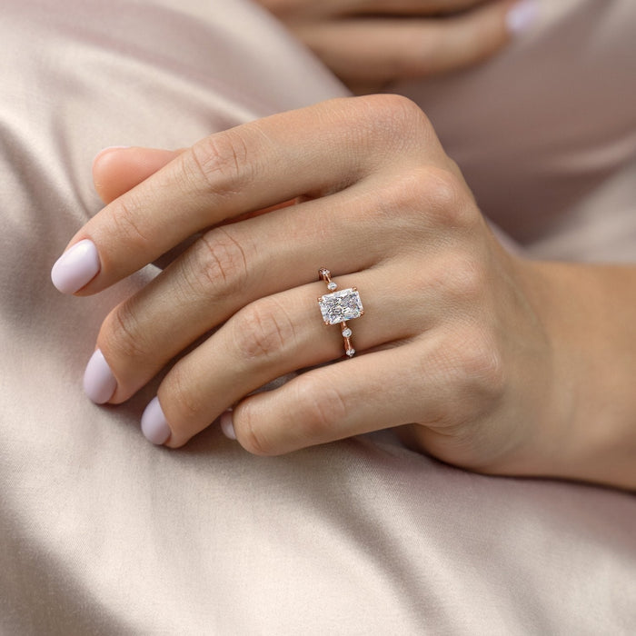 Radiant cut moissanite solitaire engagement ring with a hidden halo and a slim band with small round stones set at intervals, view 2