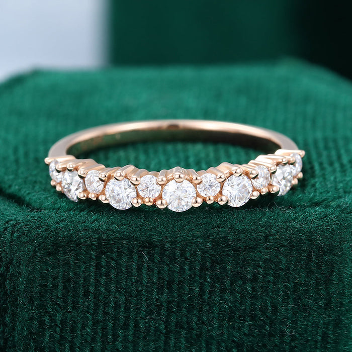 Front view of a rose gold half eternity band with larger and smaller round moissanite stones on green velvet