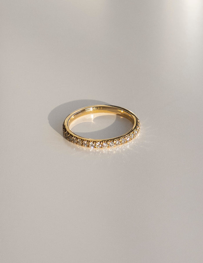 Slim gold pave half eternity wedding band with round moissanite on a light surface