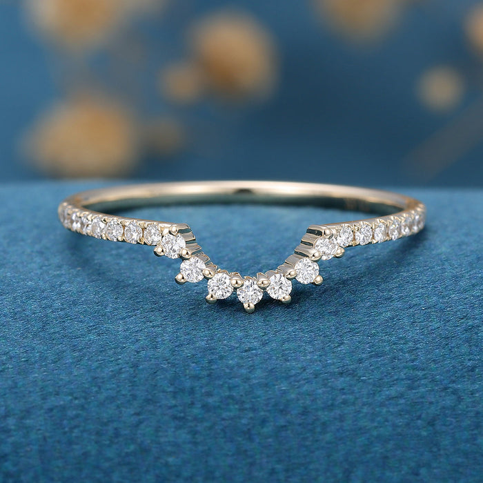 Front view of a curved wedding band with a crown of round moissanite and pave shoulders in yellow gold