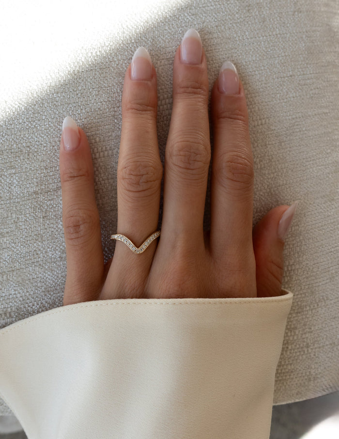 Curved V pave wedding band with moissanite worn on the ring finger, hand view