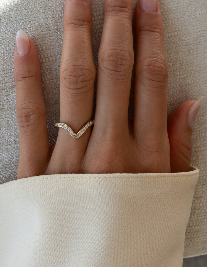 Curved V shaped pave wedding band with round moissanite worn on a finger