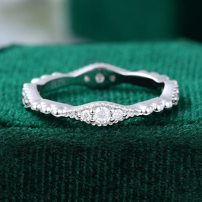 Front view of a white gold vintage wedding band with three round moissanite stones and a beaded wavy shank
