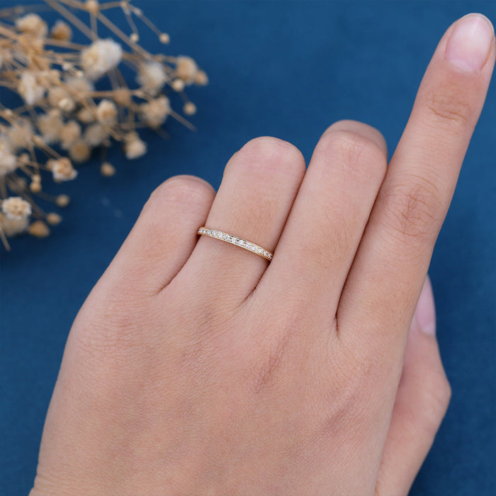 Round moissanite channel set milgrain wedding band in yellow gold worn on a finger