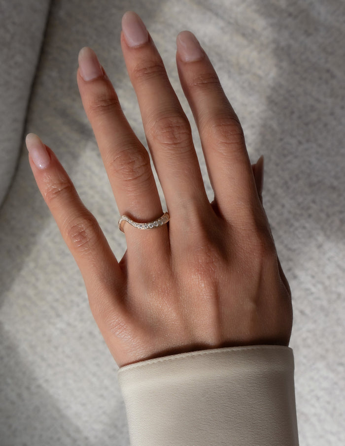 Curved wave pave wedding band with round moissanite worn on a hand