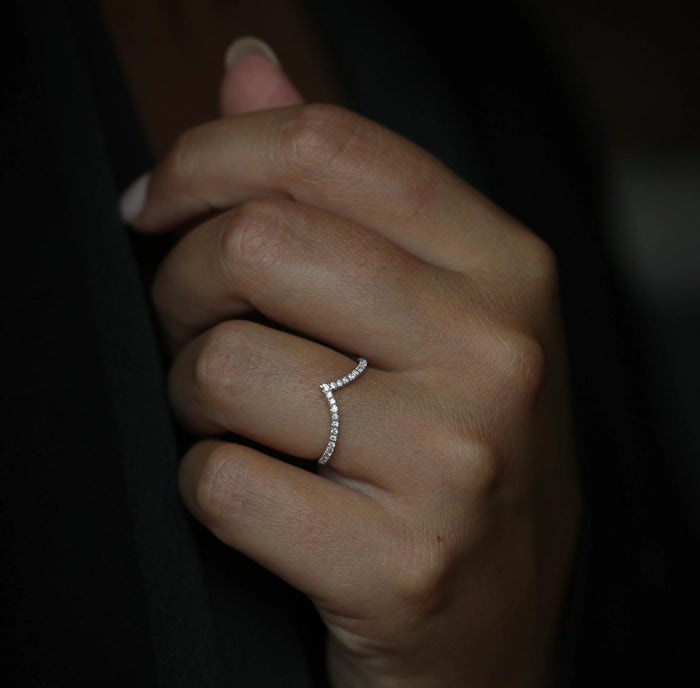 Curved V shaped moissanite wedding band in white gold worn on a finger