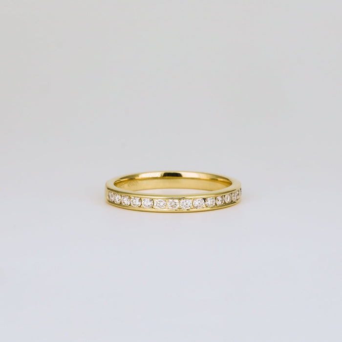 Front view of a round moissanite channel set band in yellow gold