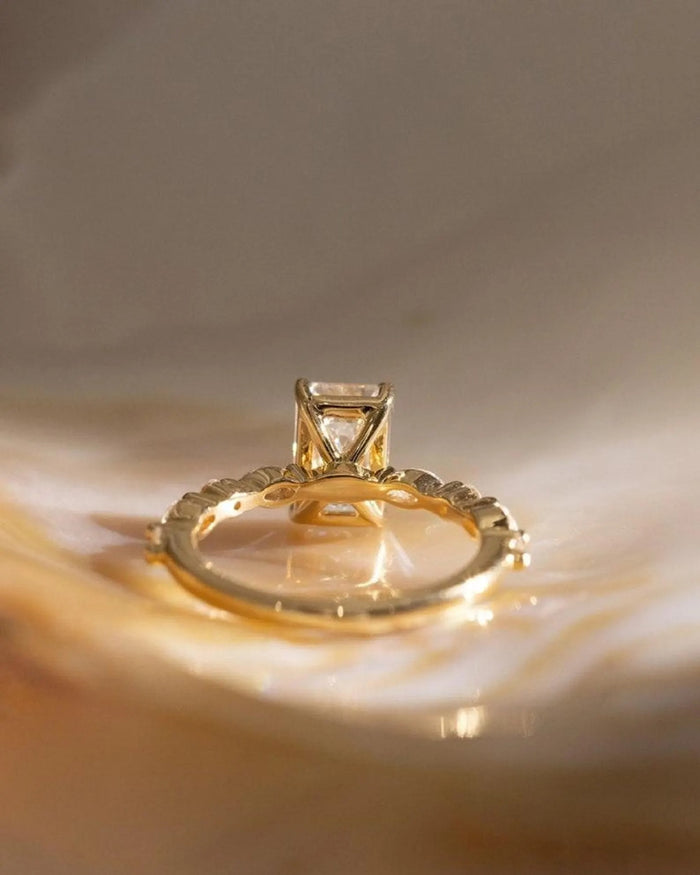 Alternating marquise and round accents along the shoulders of the emerald cut ring