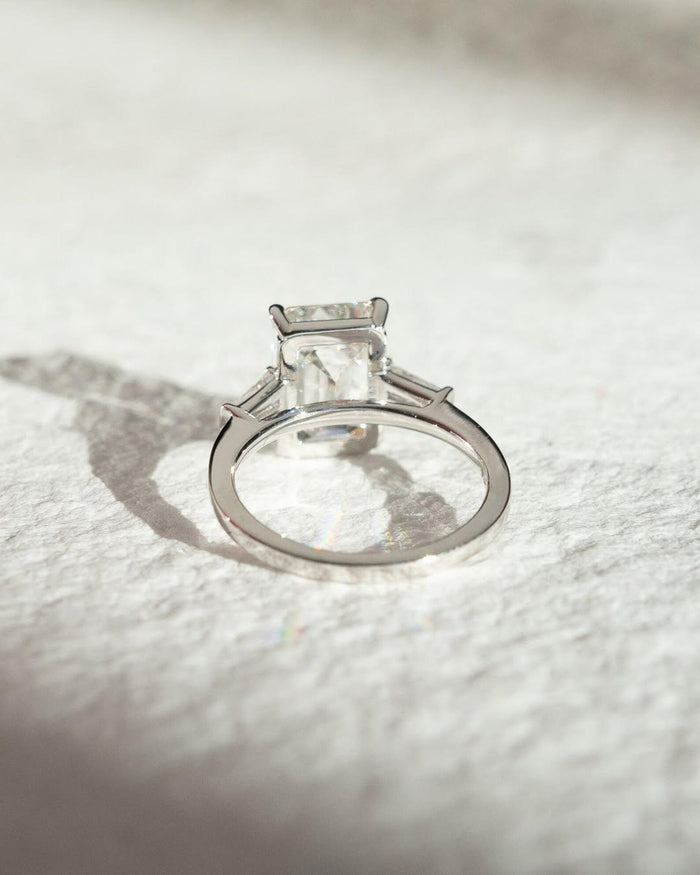 Emerald cut lab grown diamond three stone ring shown on the hand, E color VVS2 center stone