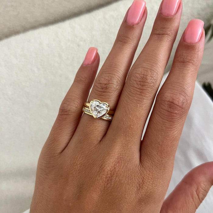 Heart shaped moissanite bezel ring and straight pave band shown on a flat hand