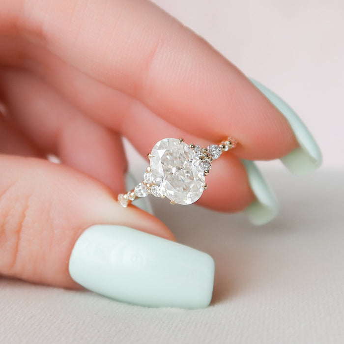 Oval cut moissanite cluster engagement ring in yellow gold held in hand
