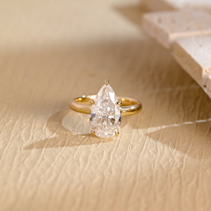 Elongated pear shaped moissanite statement solitaire engagement ring held by five slim claws on a smooth polished yellow gold band