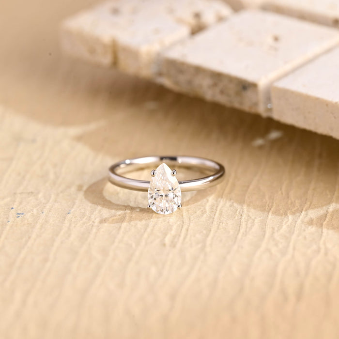 Upright pear moissanite solitaire engagement ring set point up in four slim claws on a thin polished white gold band