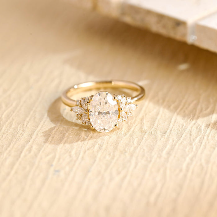 Oval moissanite engagement ring with a fan of marquise and small round stones on each side of the oval on a slim plain yellow gold band