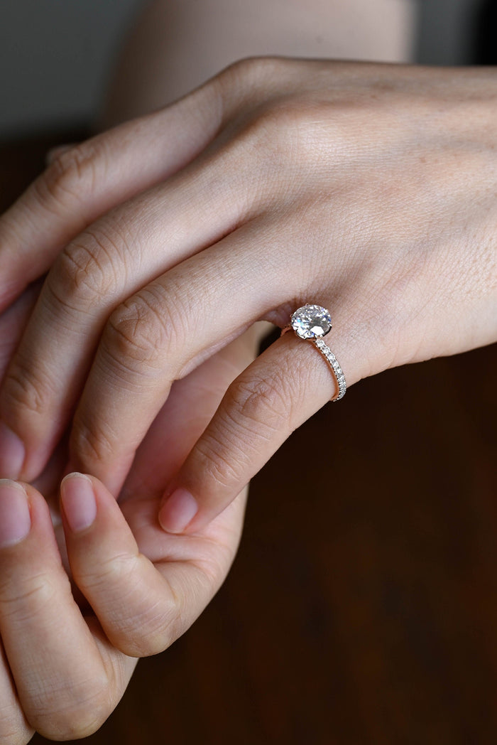 Vintage style round moissanite solitaire engagement ring with broad facets in six claws on a rose gold band pave set with tiny round stones, view 2