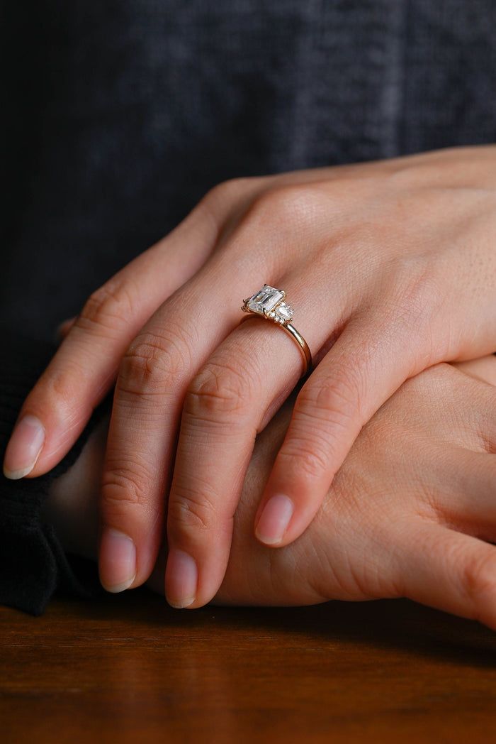 Emerald cut moissanite engagement ring with a pear and round stone cluster on each side of a plain yellow gold band, view 2